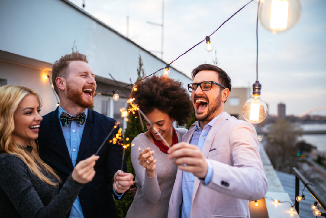 Multiracial and multi gender group of four friends at a rooftop party hold sparklers