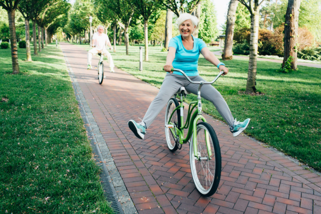 Happy senior couple riding their bikes in the park, playfully lifting their legs up as they ride