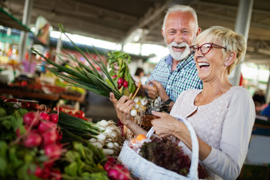 Senior couple holding vegetables and carrying basket in produce aisle of market