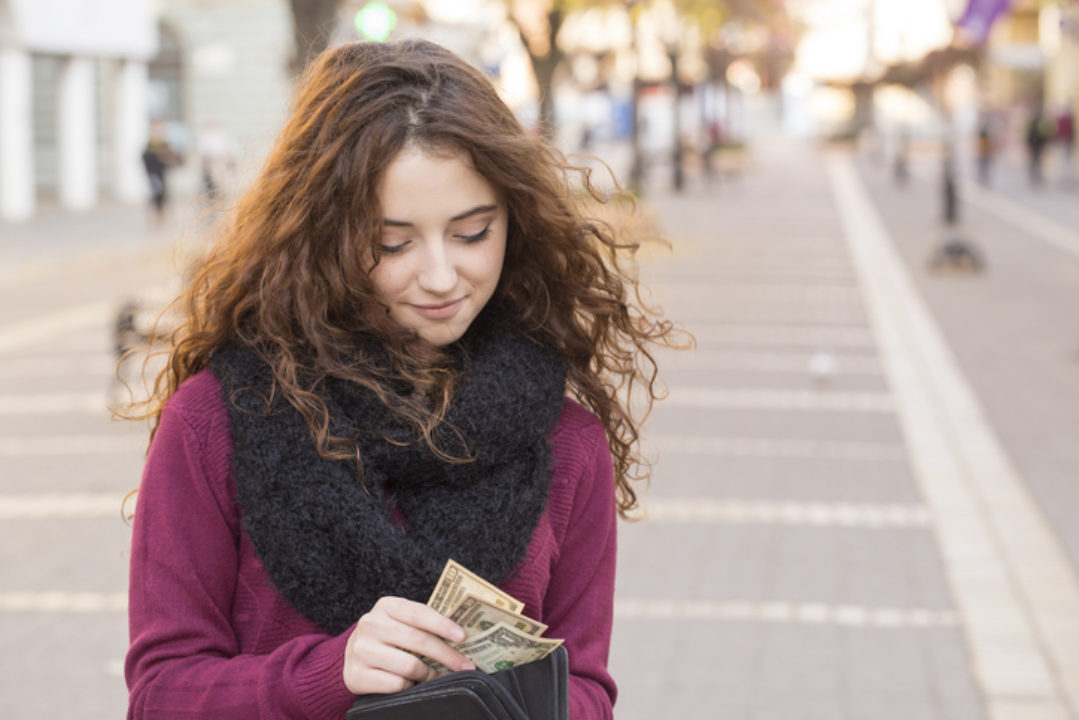 young woman shopping and taking out money from wallet on street