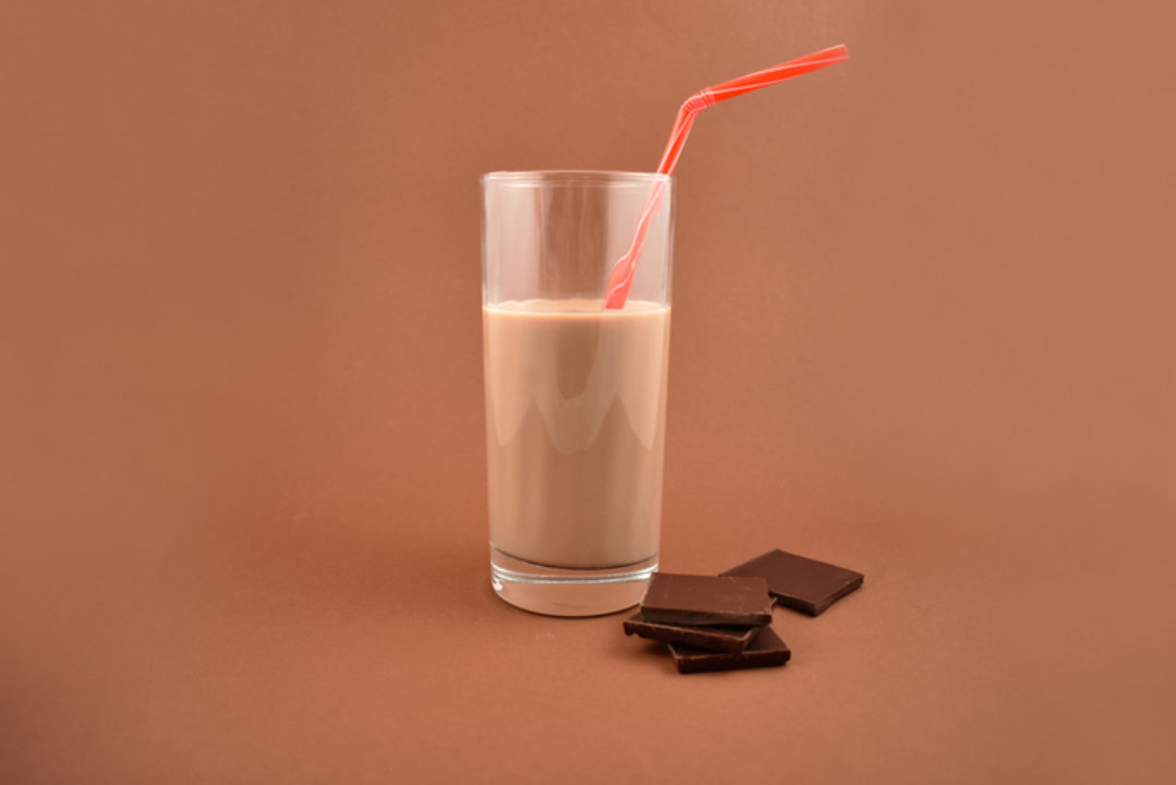 Chocolate milk with chocolate pieces. Glass of chocolate milk on a brown background.