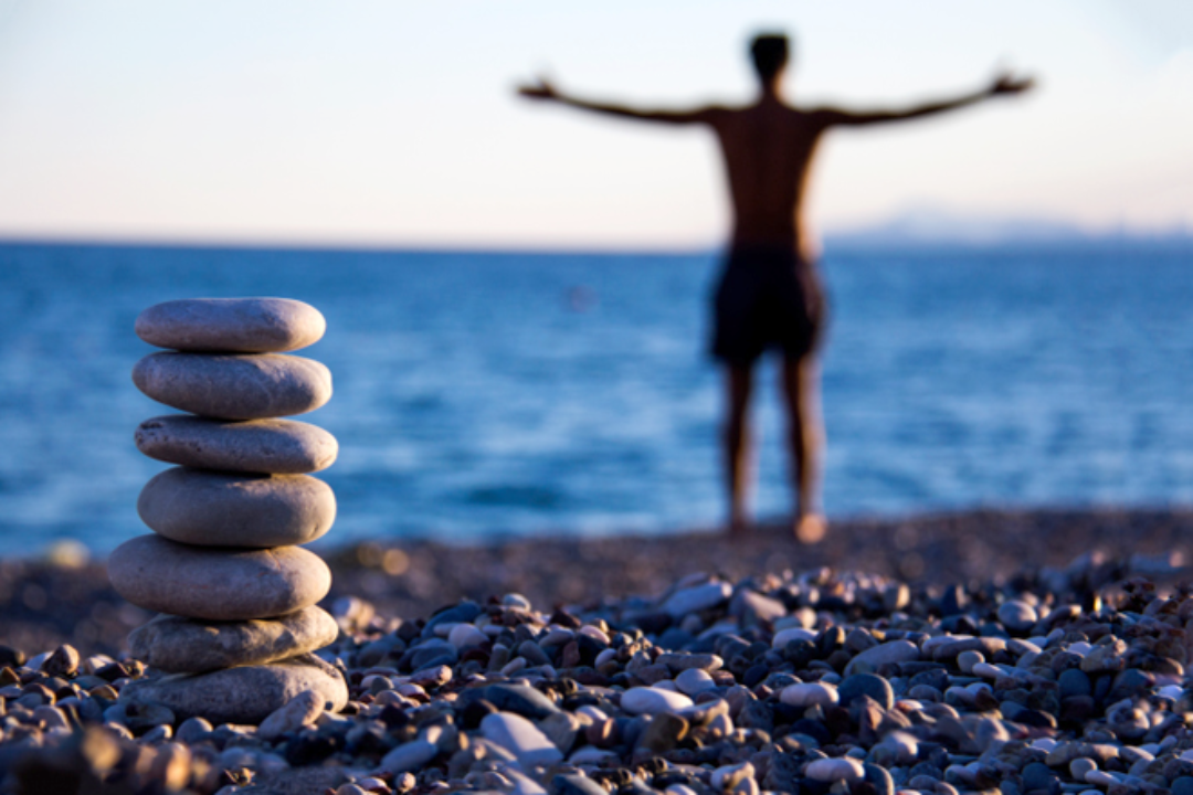 Man on beach with open arms and balancing stones