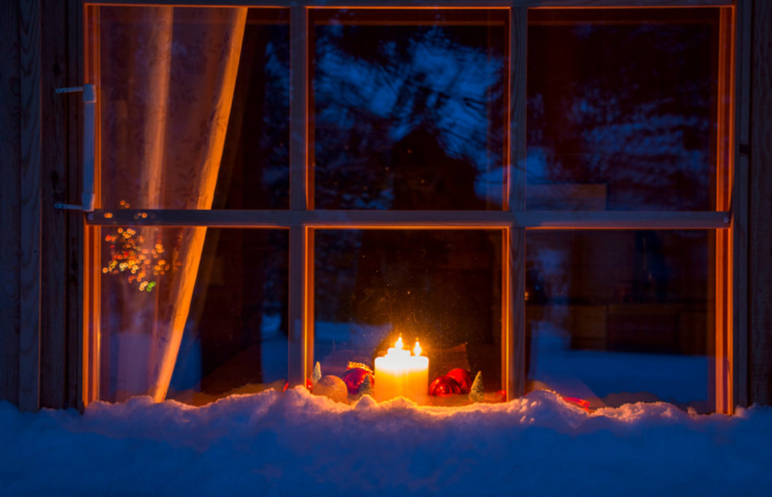 A candle burns in the window of a home on a snowy evening. 